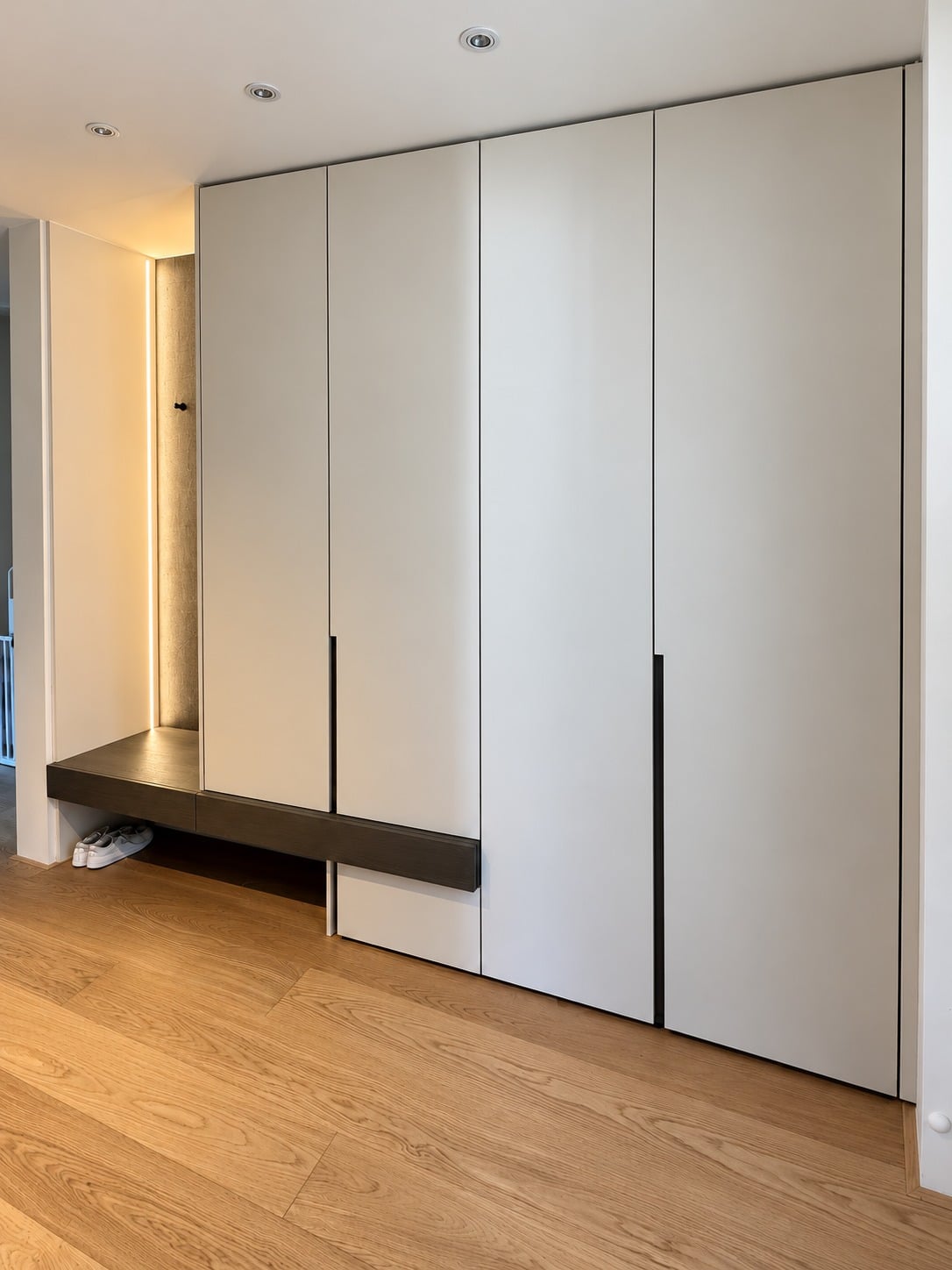 Komplette Garderobe nach Maß mit Sitzbank, hellen Schrankfronten und warm beleuchteter Nische